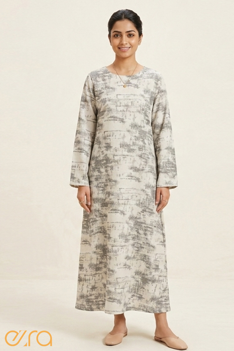 Full-length view of a woman in a long-sleeved light grey and cream maxi dress featuring a textured watercolor print and tan mules