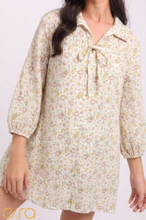 Front view of the Vintage Floral Tie-Neck Mini Shirt Dress featuring a delicate all-over ditsy floral print in shades of rose, amber, and sage on a cream base. The dress has a V-neckline with a dainty self-tie bow, a button-down bodice, and three-quarter length puff sleeves with elasticated cuffs.