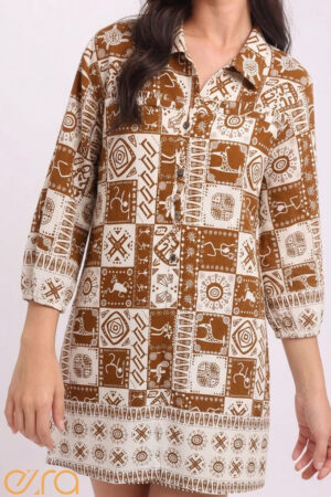 Front view of the Ezra Tribal Mosaic Tunic Dress. The dress features a structured grid pattern with hand-drawn tribal symbols, geometric suns, and animal motifs in a warm terracotta brown on a cream base. Details include a classic collar, button-down front, and three-quarter length puff sleeves.