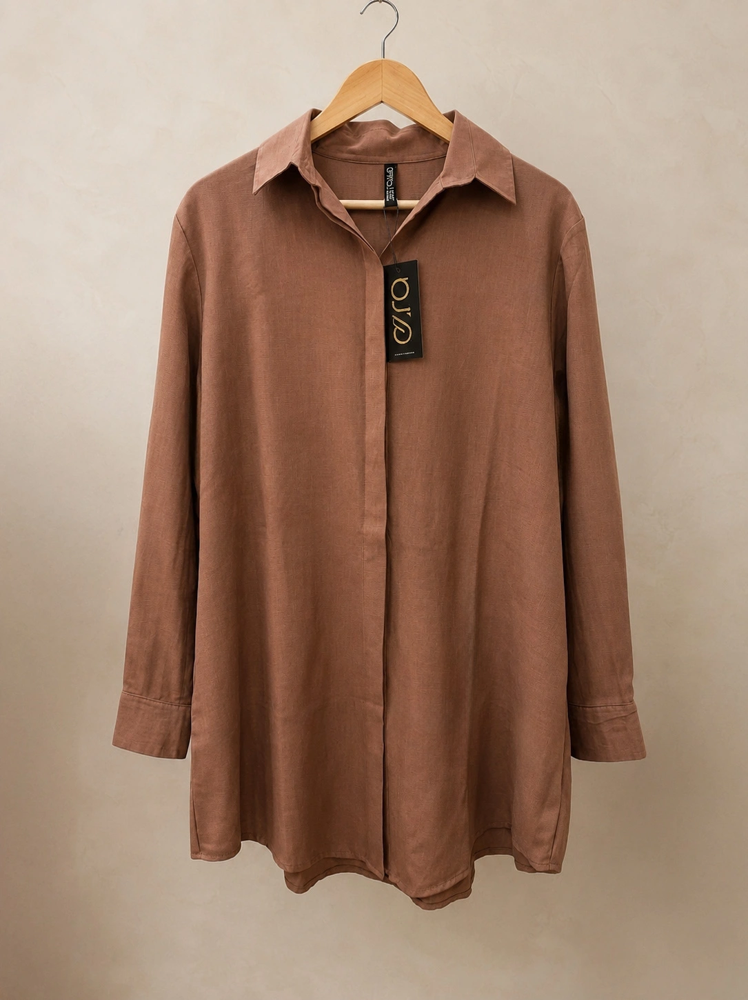 Brown long-sleeve button-down collared shirt with a hanging brand tag, displayed on a wooden hanger